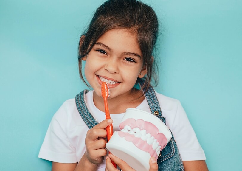 Little girl holding a red toothbrush in front of a blue backdrop